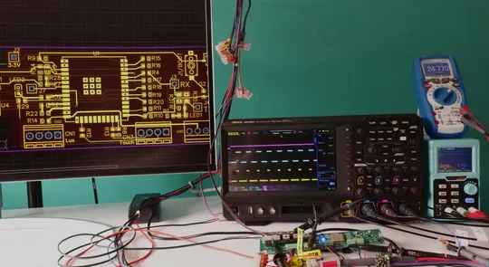 Bench under test: PCB layout on a monitor at left, oscilloscope tracing a digital bus, multimeter and bench power supply at right, and two circuit boards wired up with probe hooks and alligator clips